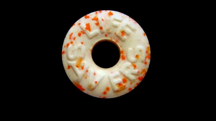 An orange-speckled Life Saver placed on a black surface.