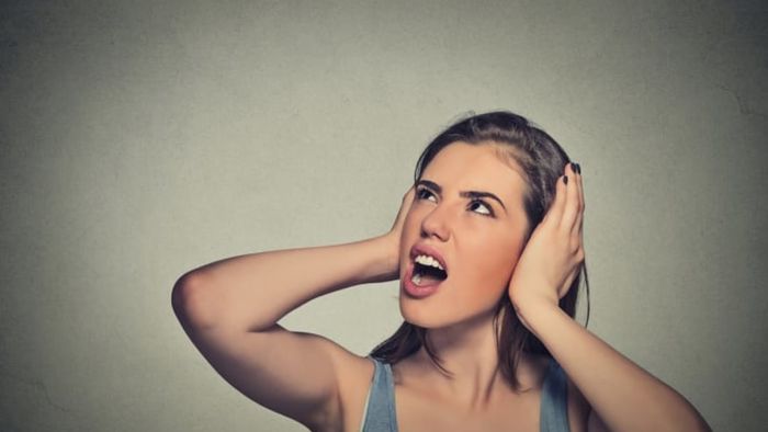 A woman covering her ears with her hands, appearing frustrated.