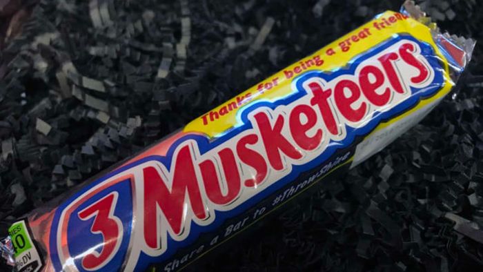 A 3 Musketeers bar resting on a black backdrop.