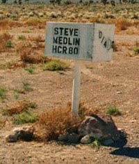 A white mailbox mounted on a white post in the desert, marked with