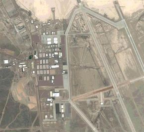 A satellite image of Area 51 reveals a stark desert landscape, intersected by roads and scattered structures.