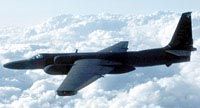 A U-2 reconnaissance aircraft soars through the sky, set against a backdrop of billowy white clouds.