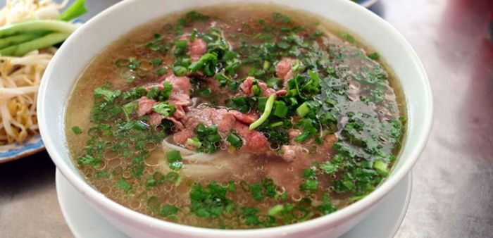 Phở bò 23 ảnh 1 - Tác phẩm nghệ thuật ẩm thực: tô phở bốc khói nghi ngút với thịt tái hồng tươi, hành lá xanh mướt điểm xuyết trên nền nước dùng vàng óng.