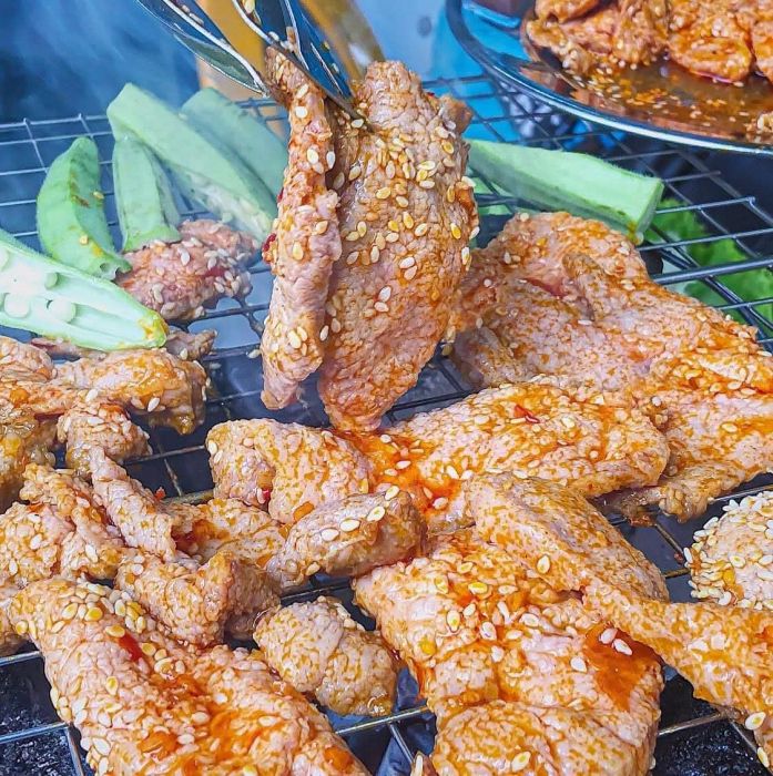Bò Nướng Ngói và Lẩu Cô Tư - Khung cảnh ấm cúng với những miếng thịt nướng vàng ruộm tỏa hương thơm phức trên bếp than hồng, điểm tô thêm nồi lẩu nghi ngút khói.
