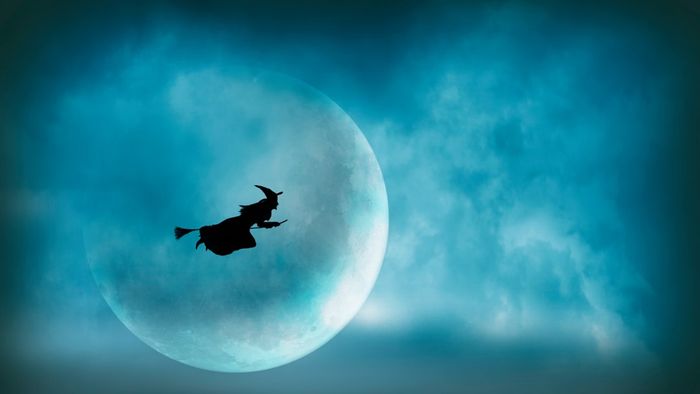 A silhouette of a witch flying on a broomstick against a moonlit backdrop.