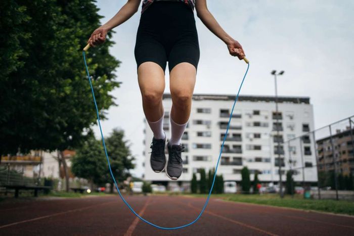 A woman jumping rope on a running track in an urban environment, viewed from the waist down.