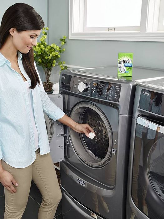 A model placing a washing machine cleaning tablet into their machine.