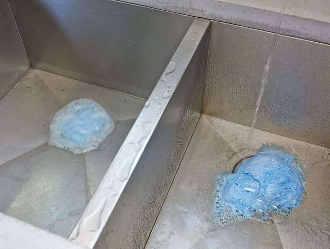 A drain with blue foaming bubbles inside, indicating the cleaning action in progress.