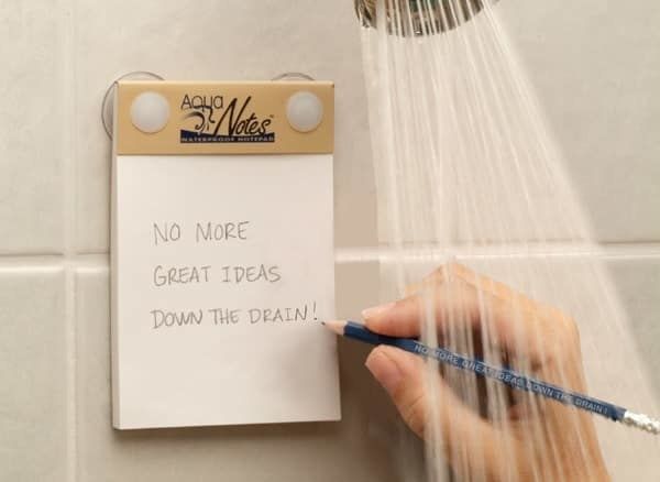 A hand writing 'no more great ideas down the drain' on the notepad while in the shower