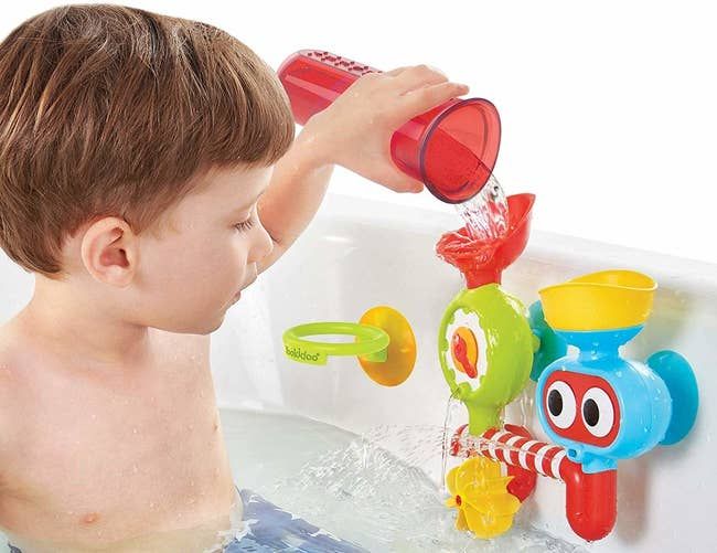 A child model happily pouring water into the multi-colored water lab while in the tub.