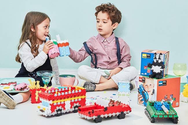 Two child models playing with colorful puzzle blocks, creating vehicles and animals.