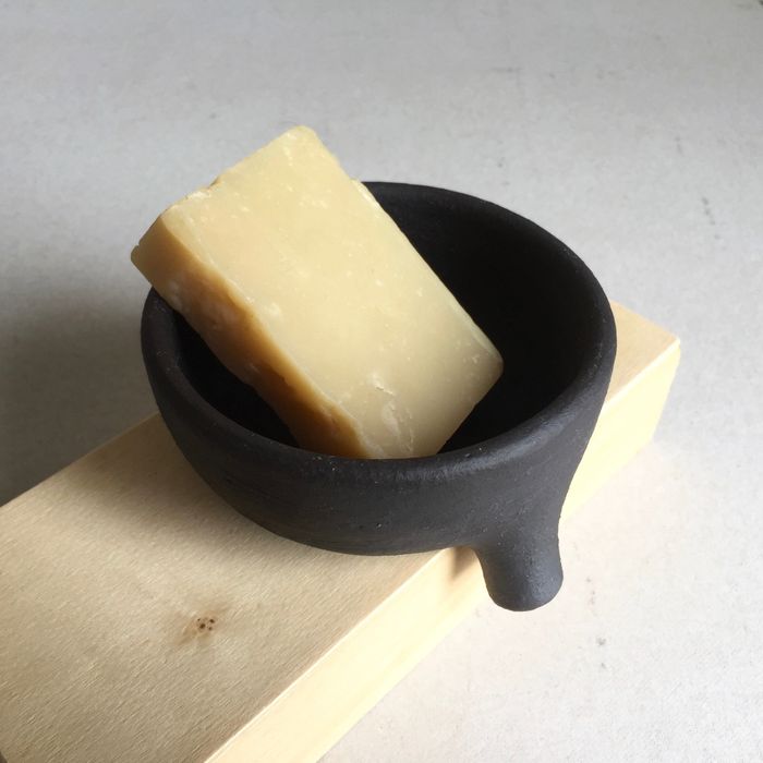 The soap dish holding a bar of soap, positioned with its drainage spout hanging over the edge of a surface.