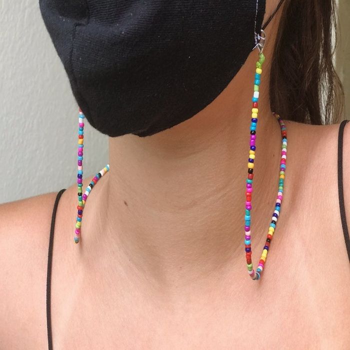A model wearing a face mask with a rainbow-colored beaded chain attached to it