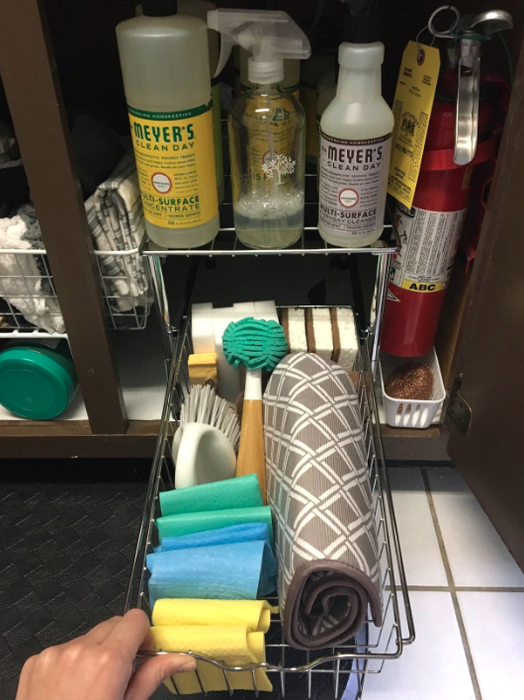 A reviewer pulls out their drawer to reveal three sponges, four magic erasers, two handheld scrub brushes, one dish brush, four folded dishcloths, and a folded drying pad all neatly arranged