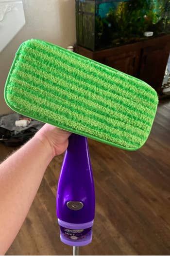 A reviewer showing off their Swiffer with the green microfiber pad attached to the bottom.