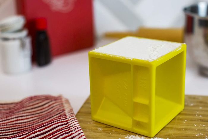 A yellow measuring cube with marked grooves, used for measuring various portions