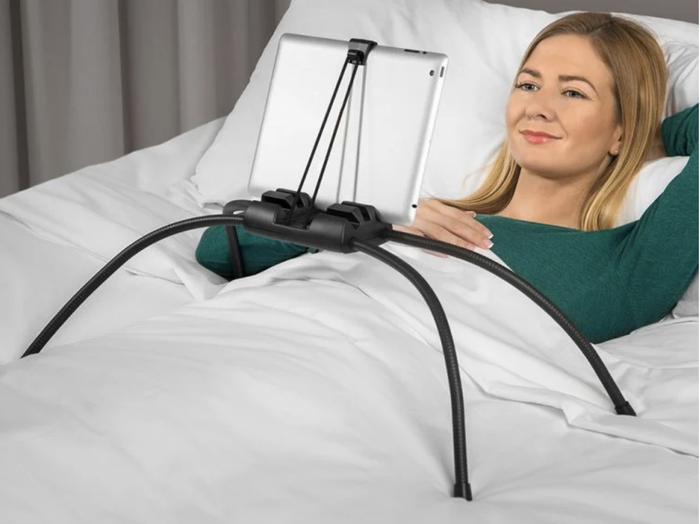 A model using the stand to comfortably watch television on their tablet from the coziness of their bed.