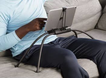 A model demonstrating the versatility of a flexible four-legged black stand, with their tablet hovering above their lap while sitting on the couch.