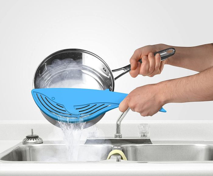 A blue whale-shaped strainer being held over a pot of pasta to drain the water.