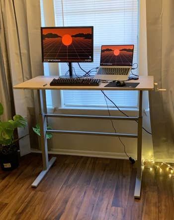 a reviewer’s photo of the desk in a raised position, holding a monitor, laptop, and keyboard