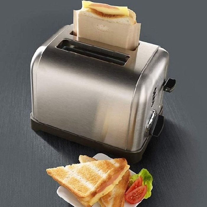 A grilled cheese sandwich inside a toaster bag, popping out of a toaster, placed next to a plate with a finished grilled cheese sandwich.