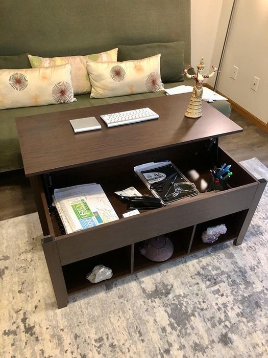 The same reviewer showing the top of the coffee table lifted toward the couch, revealing a variety of items stored inside.