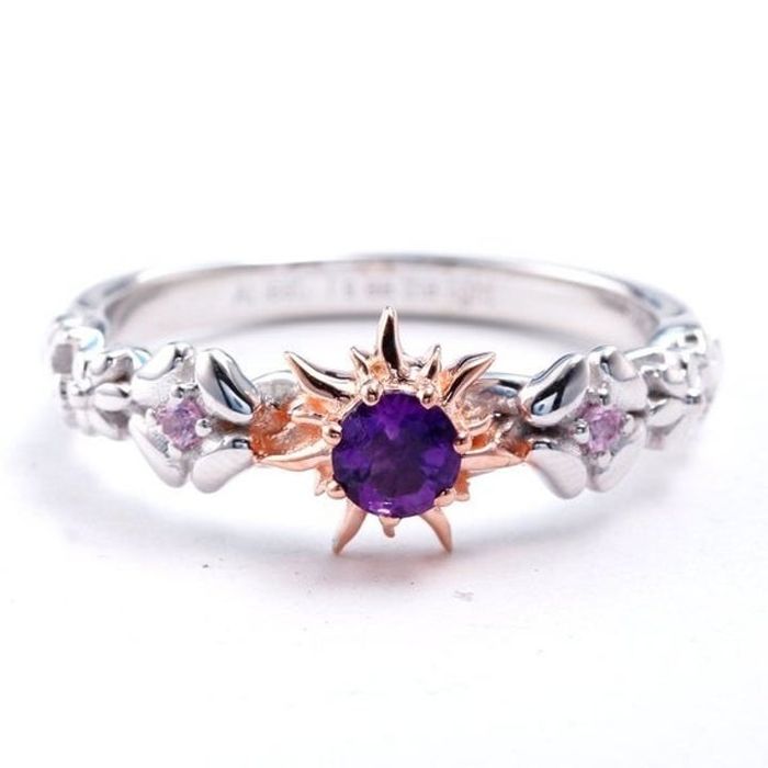 The ring featuring a central amethyst, a sunburst setting, and a band with an intricate braided floral pattern