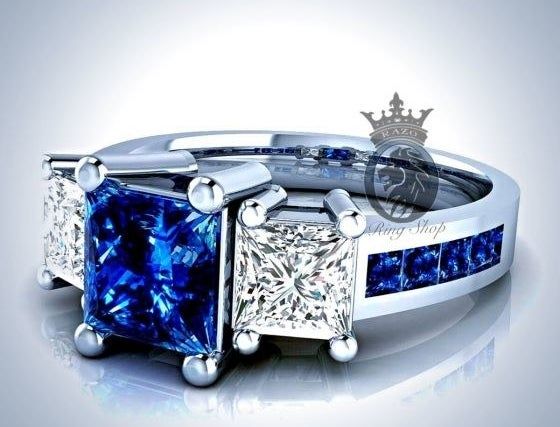 A ring showcasing a central blue sapphire accompanied by two square white diamonds, with a band adorned by smaller blue sapphires