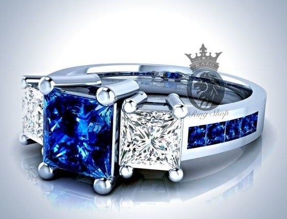A ring showcasing a central blue sapphire accompanied by two square white diamonds, with a band adorned by smaller blue sapphires