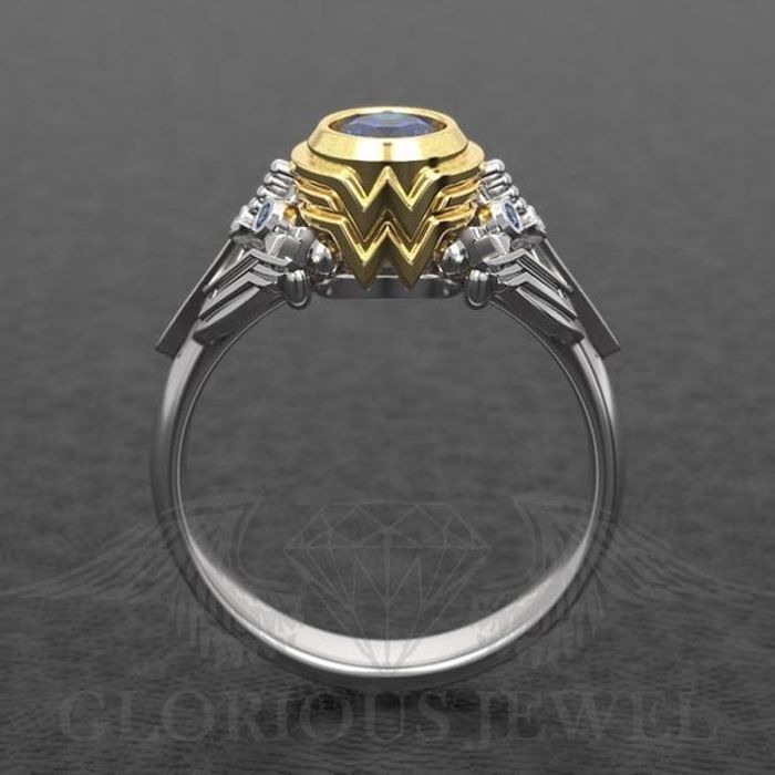 A silver ring with a blue central gemstone set in a gold frame designed to resemble the iconic Wonder Woman emblem