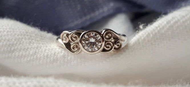 A silver ring featuring a clear gemstone and a band engraved with the Air Tribe symbol from 