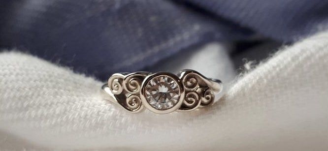 A silver ring featuring a clear gemstone and a band engraved with the Air Tribe symbol from