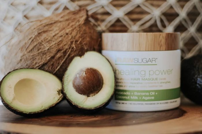 A jar of hair mask accompanied by a sliced avocado and a whole coconut