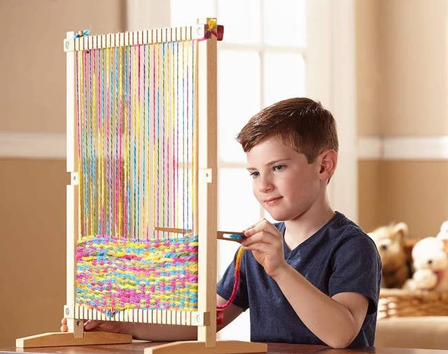 A child model engaged in playing with a loom and colorful yarn.