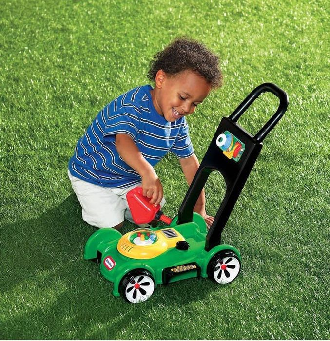 A young child, dressed in a striped shirt and white shorts, enjoys pushing a colorful toy lawn mower across a grassy lawn.