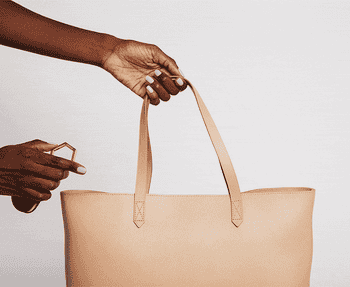 A gif of a model attaching the luggage tag to a tote and clipping a wide-brim hat to it.