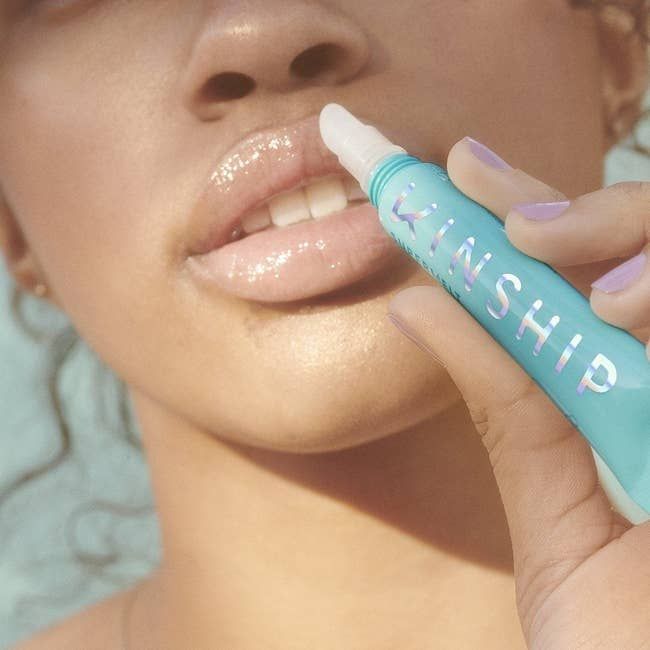 Model applying a blue tube of lip plumper to her lips
