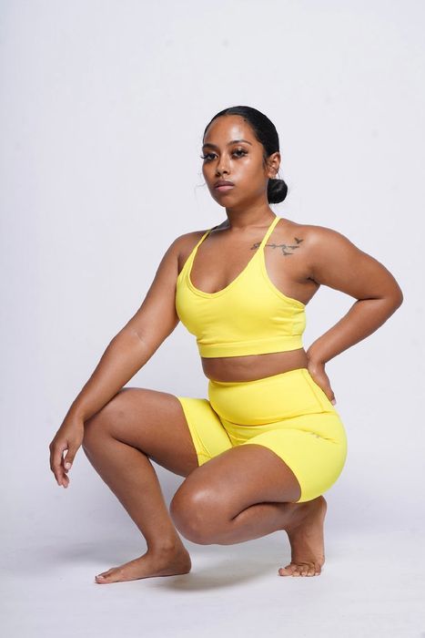 A model wearing a vibrant yellow matching biker shorts and sports bra, photographed against a white background