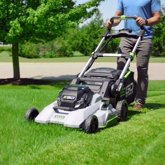 A person is seen operating a cordless, electric lawn mower on a grassy yard.