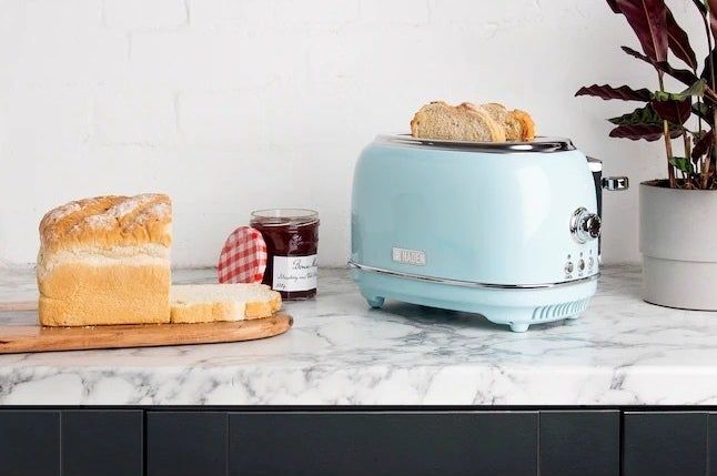 A toaster containing two slices of bread, positioned beside a bread loaf and a jar of jam.
