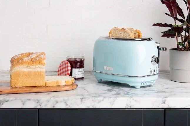 A toaster containing two slices of bread, positioned beside a bread loaf and a jar of jam.
