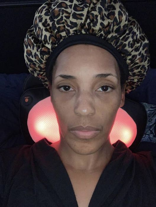 A reviewer using a red-lit massager positioned on the back of their neck for relaxation.