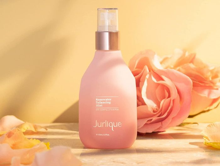 A pink bottle of skincare product surrounded by pink roses.