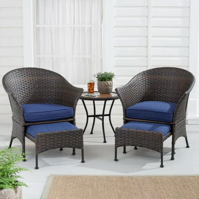 the dark wicker chairs, table, and ottomans, all featuring dark blue cushions, placed in a beautifully decorated outdoor space