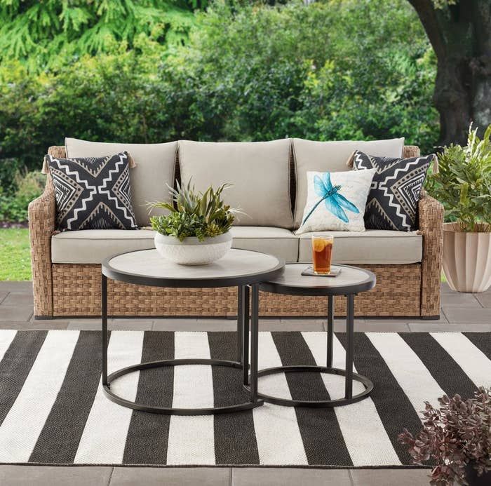 the wicker sofa with tan cushions and round nesting tables arranged in a stylish patio setting