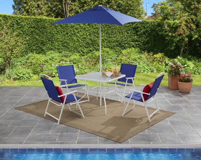 the white and blue chairs surrounding a glass table, complemented by a blue umbrella on a well-decorated poolside deck