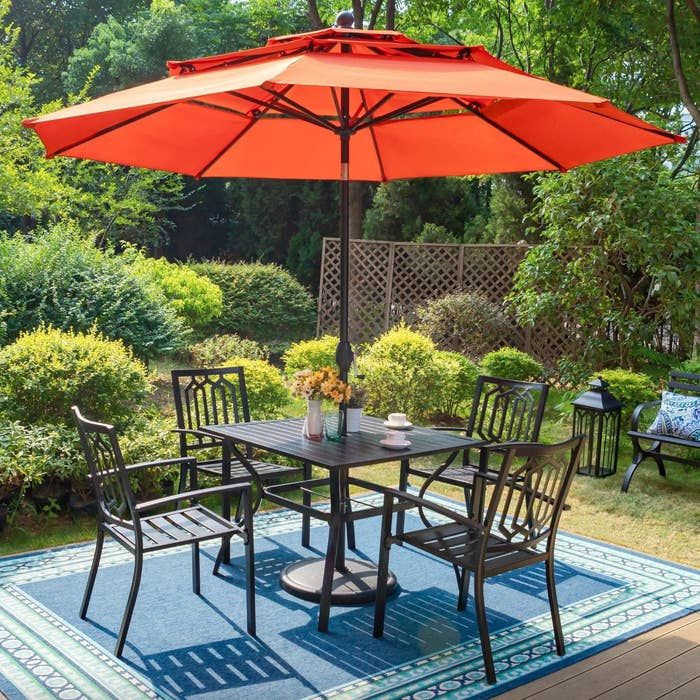 the dark metal table and chairs beneath a large orange umbrella in a beautifully decorated patio area