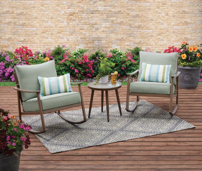 the light green cushioned rocking chairs paired with a small brown side table set against a beautifully decorated patio backdrop
