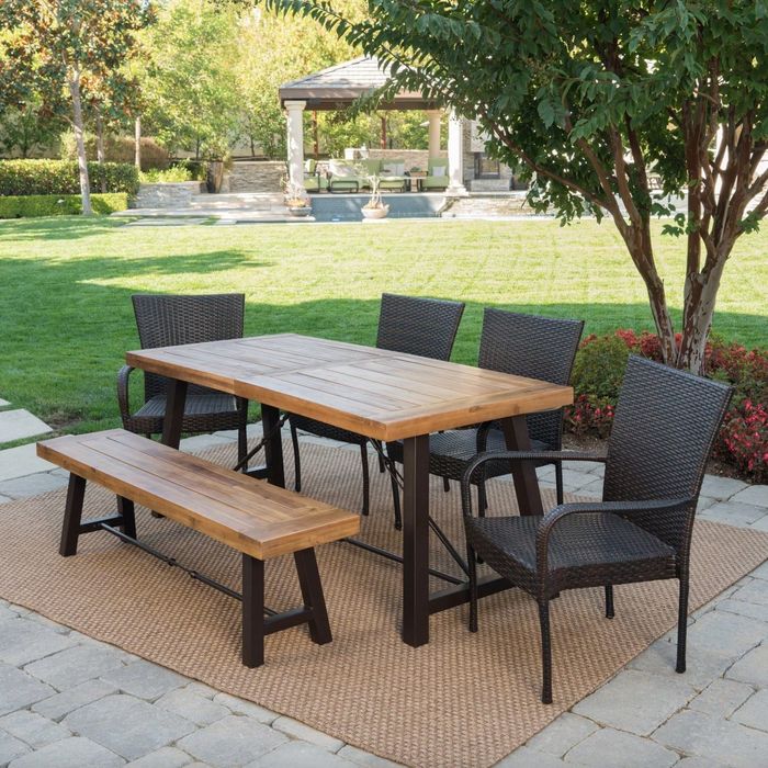 the light wood table and bench paired with dark wicker chairs in an elegantly decorated patio setting