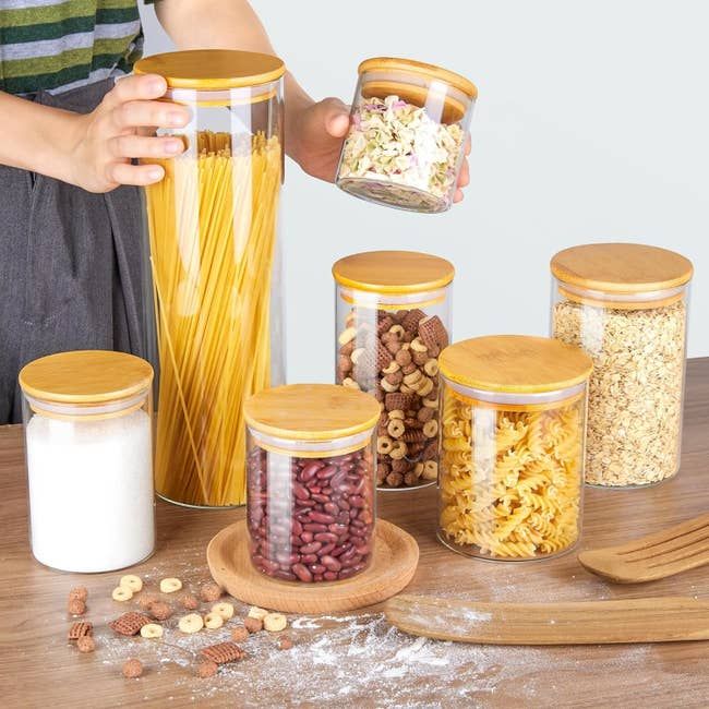 Seven glass jars in various sizes, each with a bamboo lid.